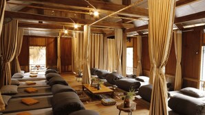 Una habitación con varias camas dispuestas en fila, vigas de madera en el techo y cortinas en las ventanas.