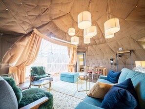Un hébergement sous tente doté d’un coin salon confortable, d’une table à manger et de lampes suspendues.