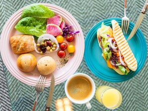 Une table mise pour le petit-déjeuner avec une assiette de nourriture, un sandwich, une tasse de café et un verre de jus de fruits.