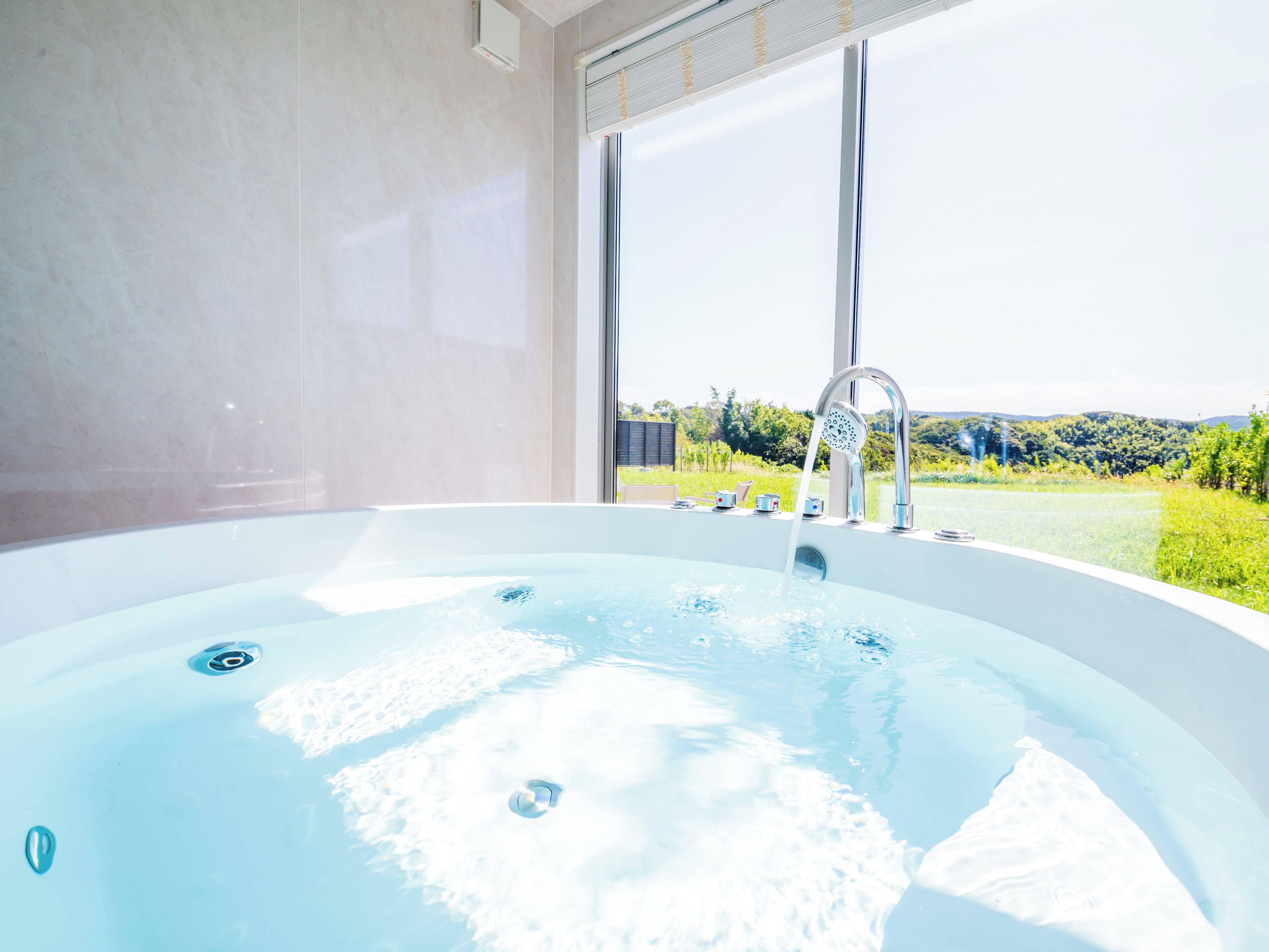 A modern bathroom with a large bathtub, a window with a view of greenery, and a built-in shower.