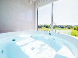 Un baño moderno con una bañera grande, una ventana con vistas a zonas verdes y una ducha integrada.