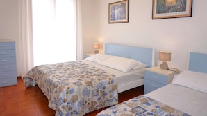 Une chambre avec deux lits, une table de chevet avec une lampe, une commode et deux tableaux encadrés au mur.
