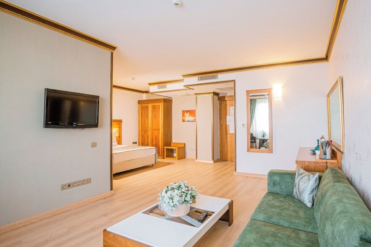 Una habitación de hotel moderna con un televisor de pantalla plana, un sofá verde, una mesa de centro de madera y una cama con cabecera de madera.