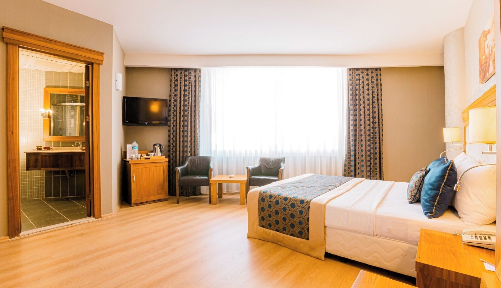 Hotelkamer met een bed, bureau, stoel, televisie en een badkamer zichtbaar door een geopende deur.