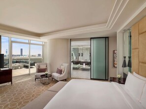 A hotel room with a large bed, a seating area with chairs, a small table, and a view of the city through large windows. - Sofitel Riyadh Hotel & Convention Centre (Riyadh)