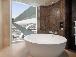 A modern bathroom with a large freestanding bathtub, a glass shower enclosure, and a view of a bridge and cityscape. - Sofitel Riyadh Hotel & Convention Centre (Riyadh)