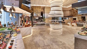 A modern hotel lobby with a central spiral staircase, a buffet area with various food options, and a spacious layout with high ceilings and contemporary lighting fixtures. - Sofitel Riyadh Hotel & Convention Centre (Riyadh)