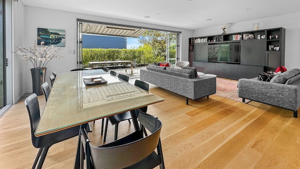 A modern living room with a glass dining table, grey sofas, and a flat-screen TV. - Orakei Oasis l Quality 3 Bed House inc. Views (Auckland)