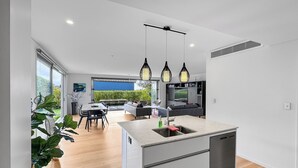 A modern kitchen with a central island, pendant lighting, and a dining area with a view of the outdoors. - Orakei Oasis l Quality 3 Bed House inc. Views (Auckland)