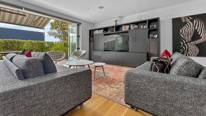 A modern living room with grey sofas, a flat-screen TV, and a bookshelf. - Orakei Oasis l Quality 3 Bed House inc. Views (Auckland)