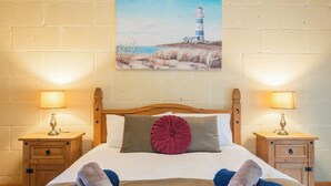 A neatly made bed with a pillow, two bedside tables with lamps, and a painting of a lighthouse on the wall. - Ellie Boo - Farmhouse w/ Pool, Hot Tub, Games Room (Xewkija)