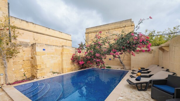 A swimming pool with lounge chairs and a flower bush. - Ellie Boo - Farmhouse w/ Pool, Hot Tub, Games Room (Xewkija)