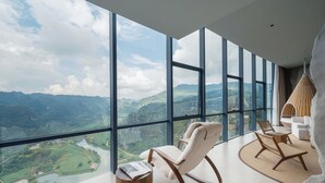 A modern interior with large windows offering a view of a mountainous landscape. There are two rocking chairs and a small wooden table. - Z-Cliff Hotel (Qianxinan Buyei and Miao)