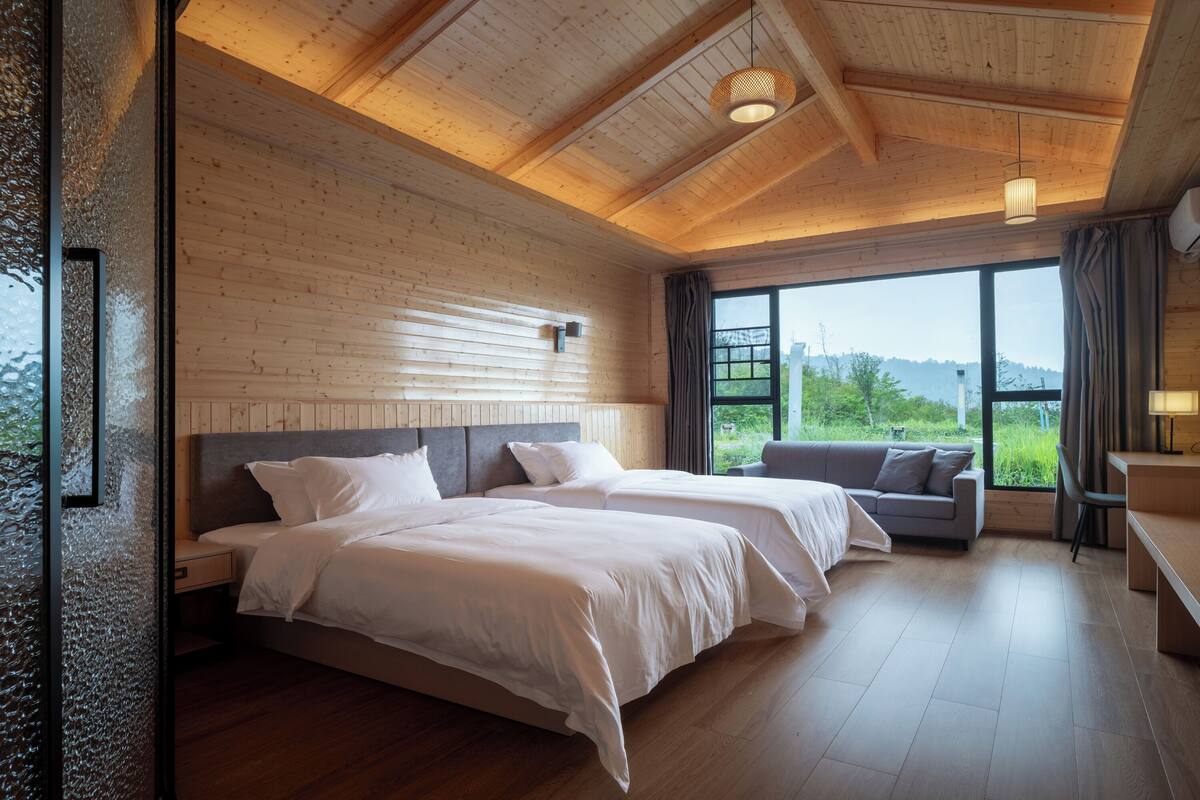 A bedroom with two beds, a sofa, and a large window with a view.