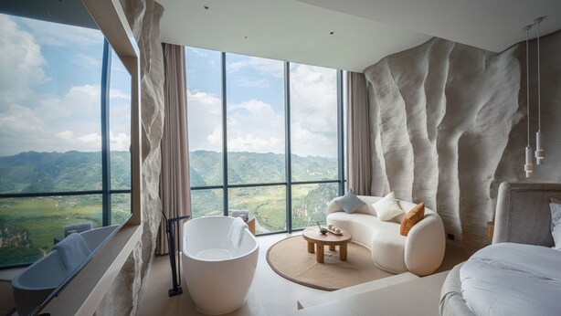A modern bedroom with a large window, a bathtub, a sofa, and a round coffee table. - Z-Cliff Hotel (Qianxinan Buyei and Miao)