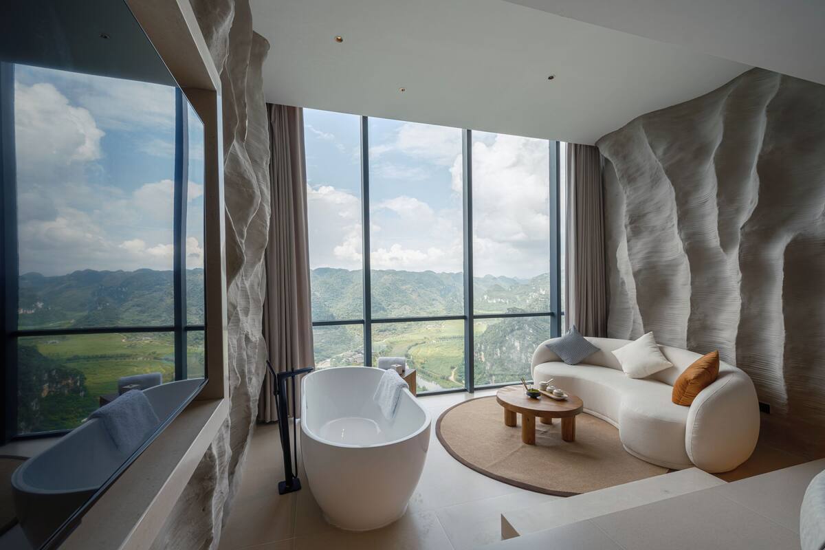 A modern room with a large window, a bathtub, a sofa, and a small table.