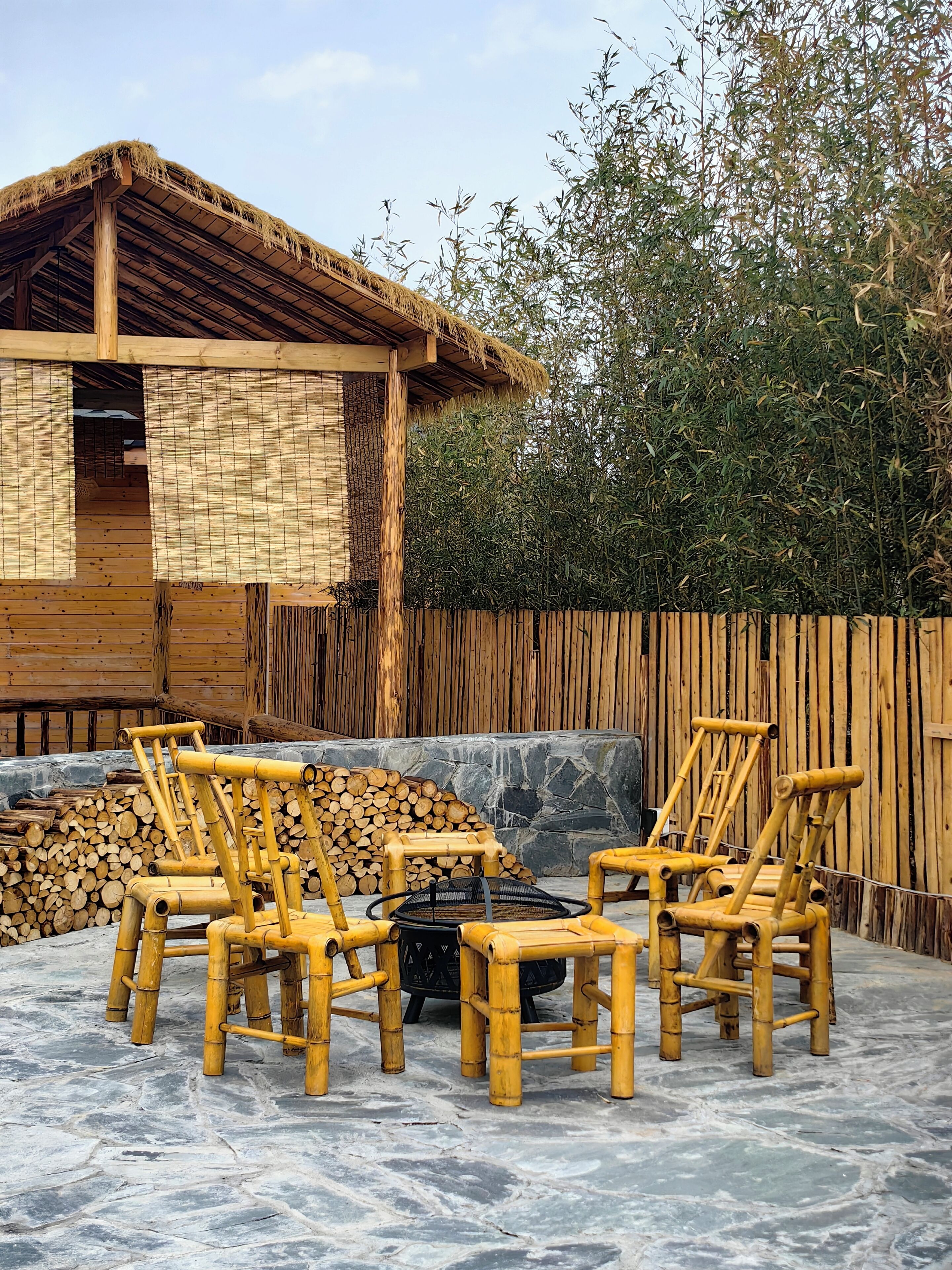 Ein draußen stehendes Set aus Bambusstuhl und -tisch, mit einem Gebäude mit Reetdach im Hintergrund.