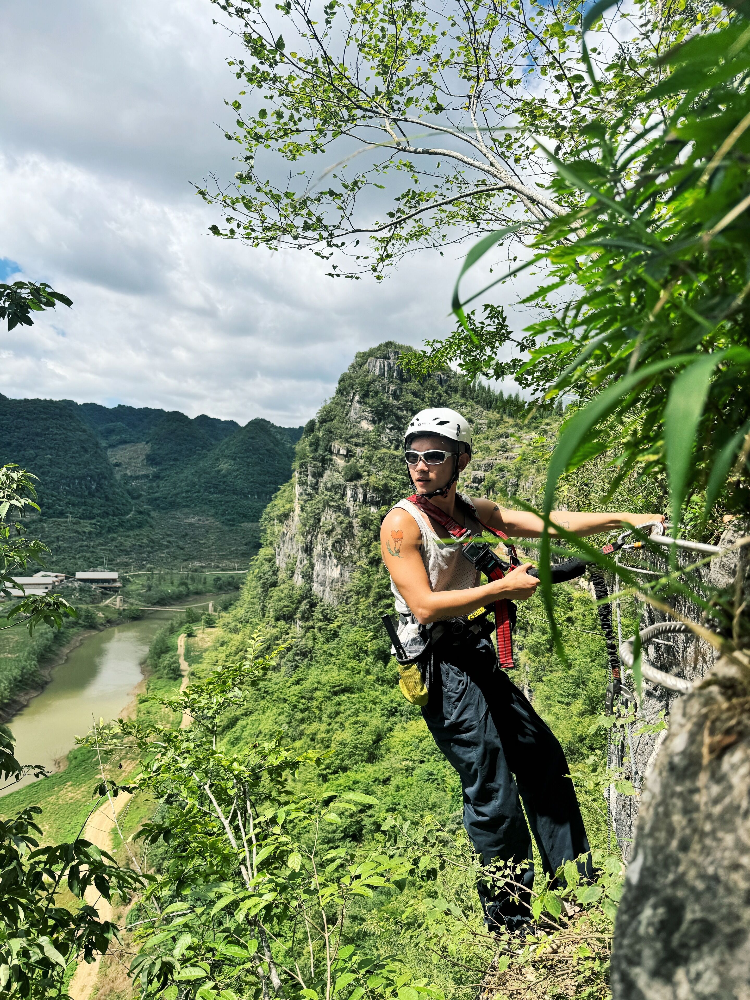 Una persona descendiendo en rappel por un risco, con un río y montañas al fondo.