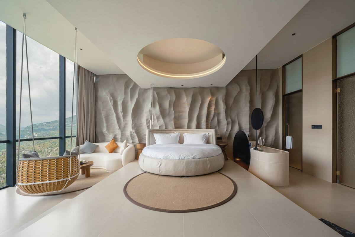 A modern bedroom with a large bed, a hanging chair, and a view of the mountains.