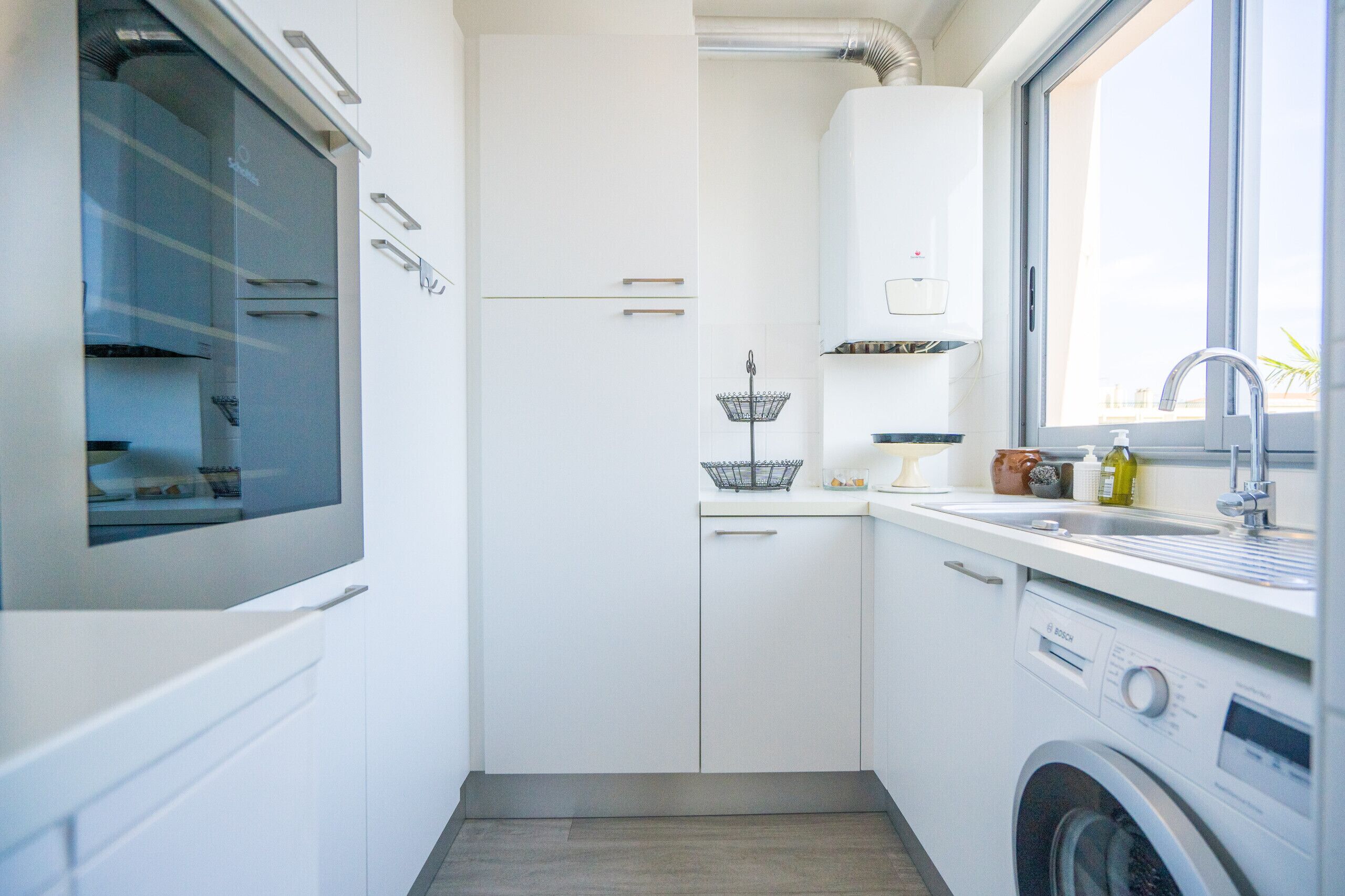 Een compacte keuken met een ingebouwde wasmachine, een raam en een spoelbak.
