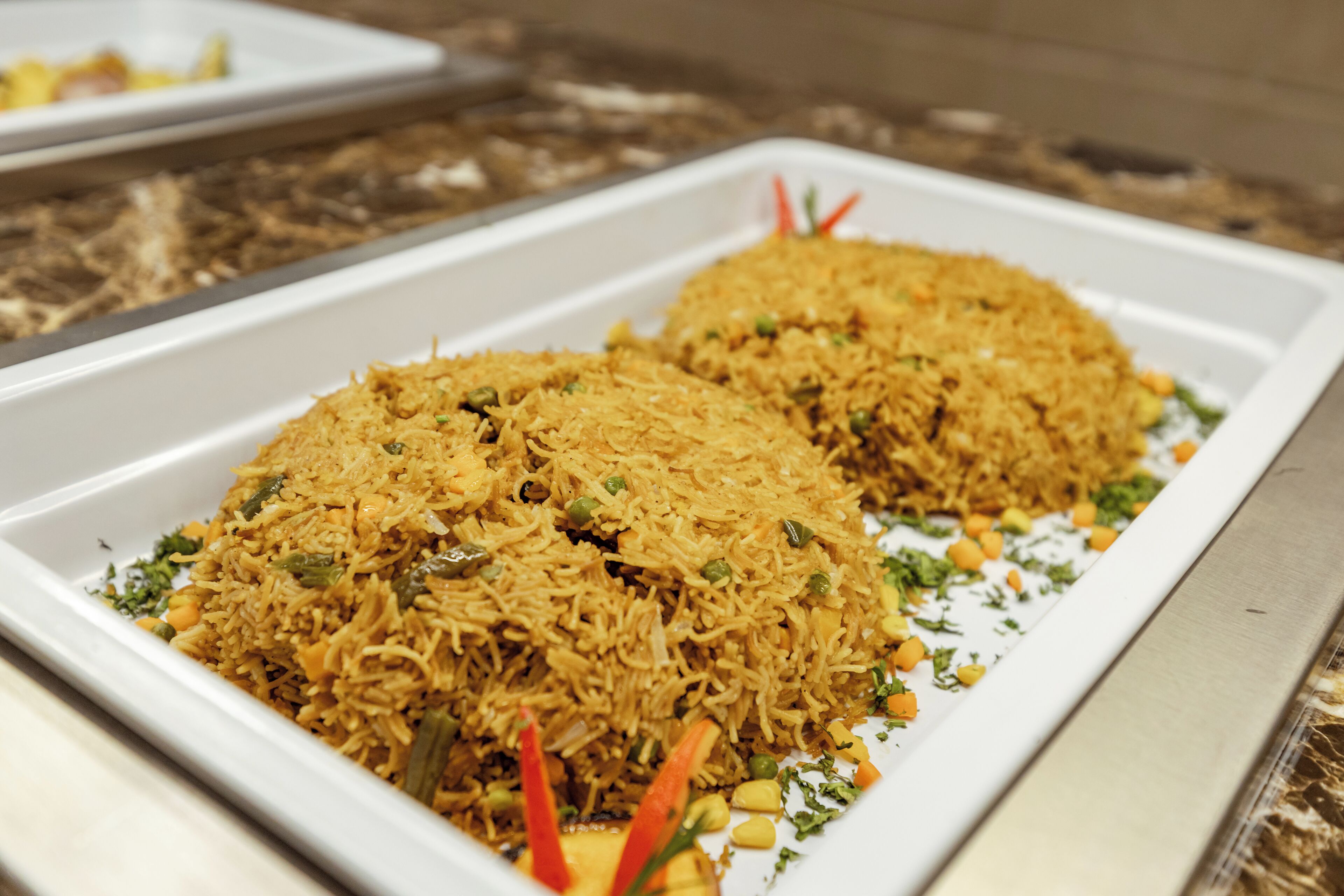A rectangular white serving dish containing a rice dish with vegetables and garnishes.