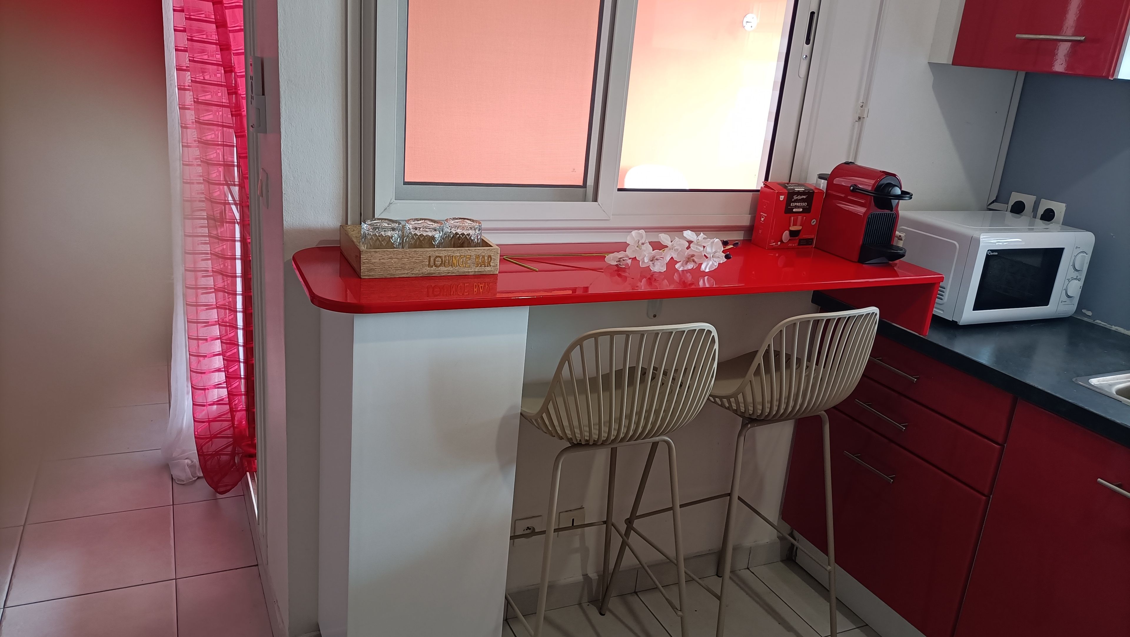 A kitchen with a red countertop, two white chairs, a microwave, and a red coffee machine.