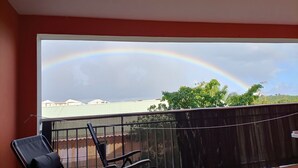 A balcony with a view of a rainbow and a distant building.