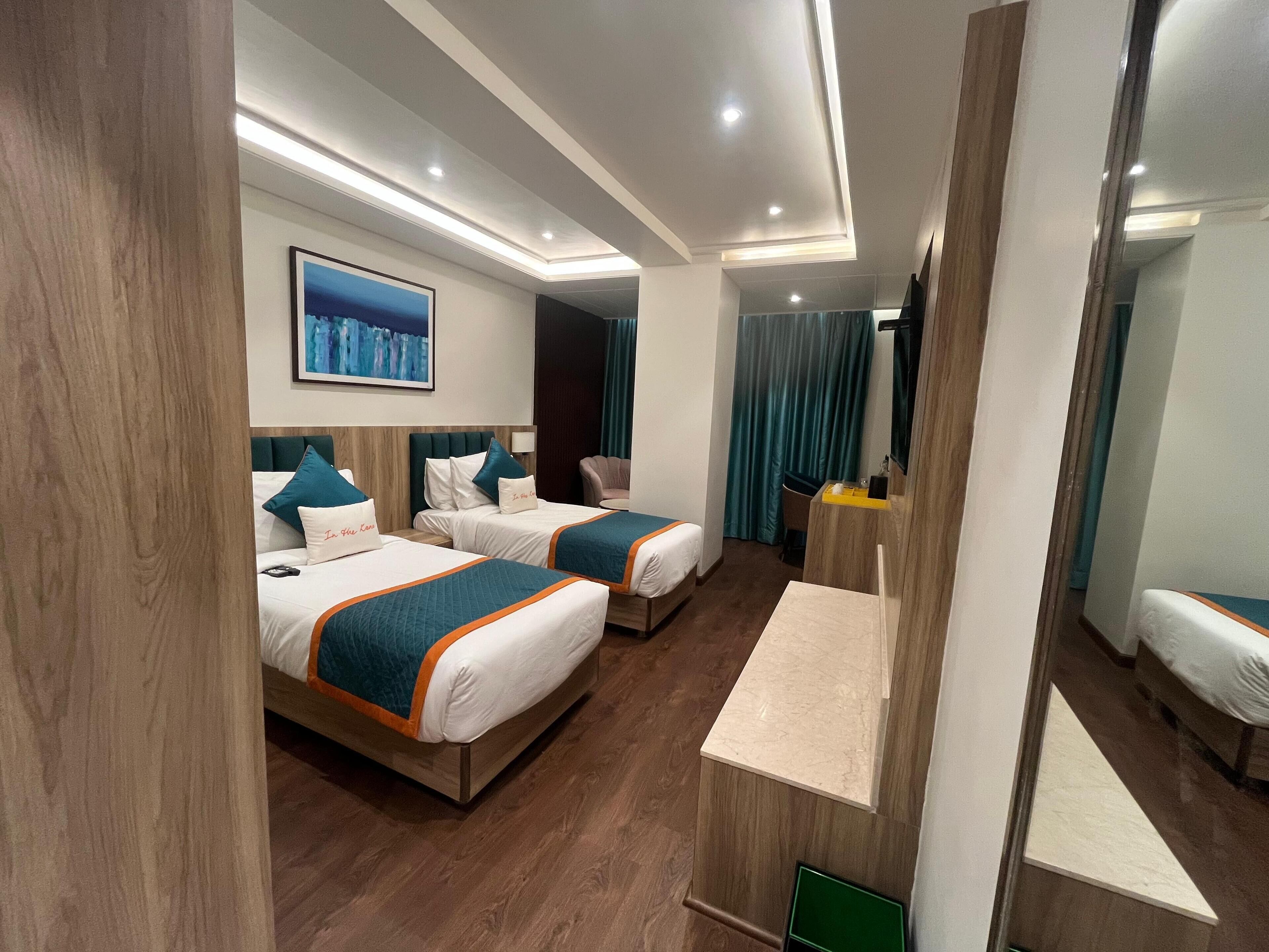 Habitación de hotel con dos camas, un escritorio, un espejo y un cuadro en la pared.