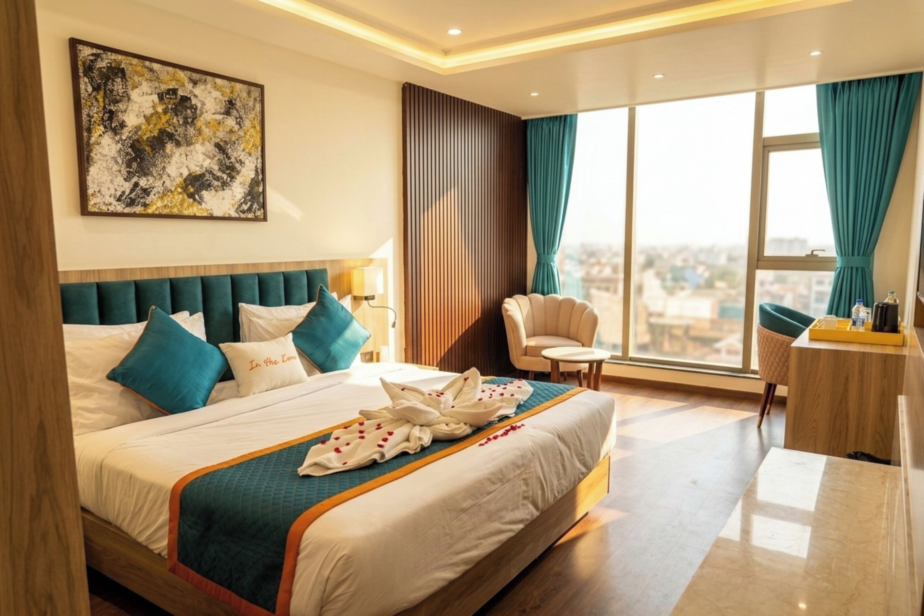 A hotel room with a large bed, a sitting area with a chair and a small table, a large window with curtains, and a city view.
