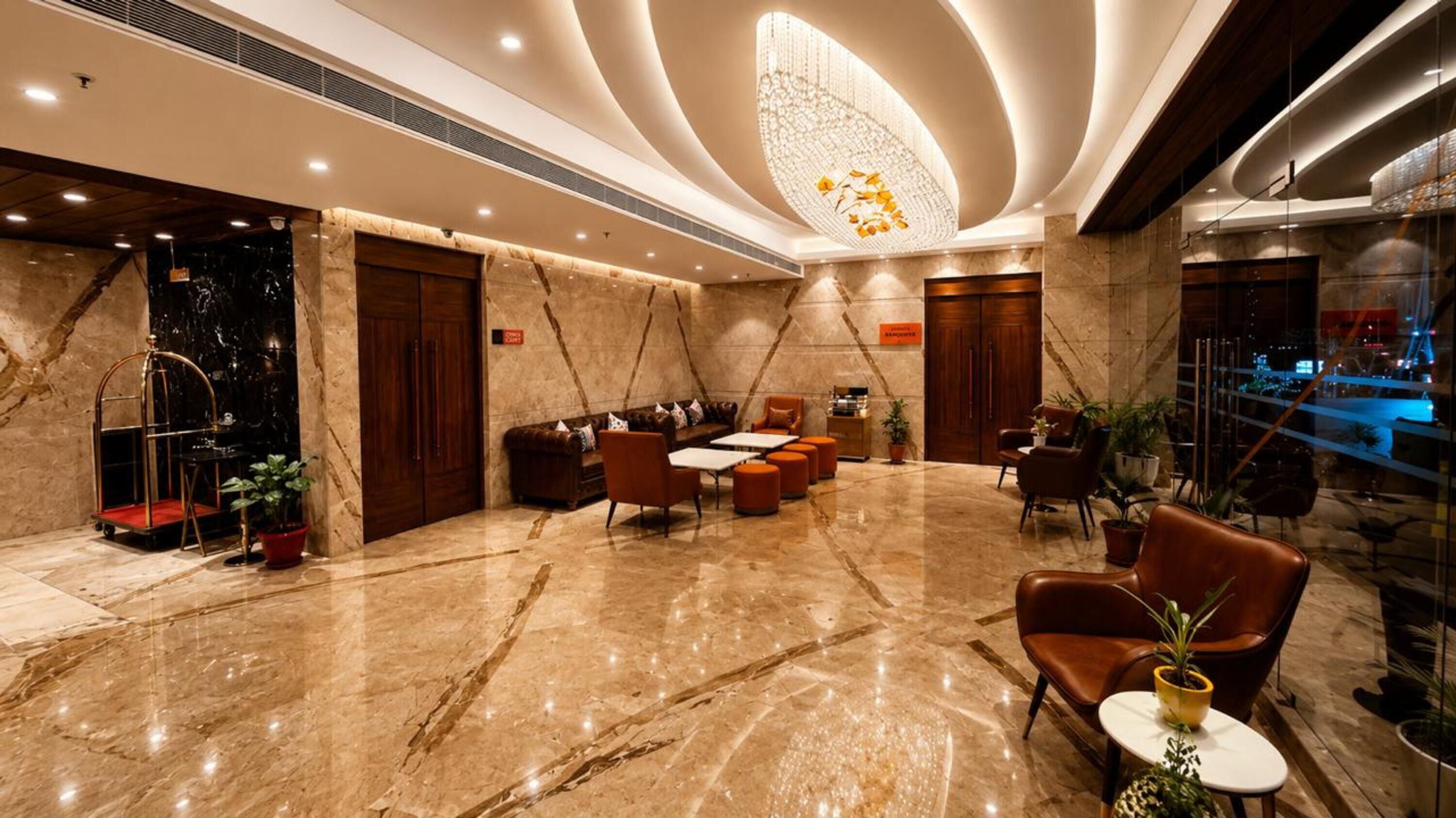 Um hall com piso de mármore, assentos de couro, um candelabro e vista da cidade através de um painel de vidro.