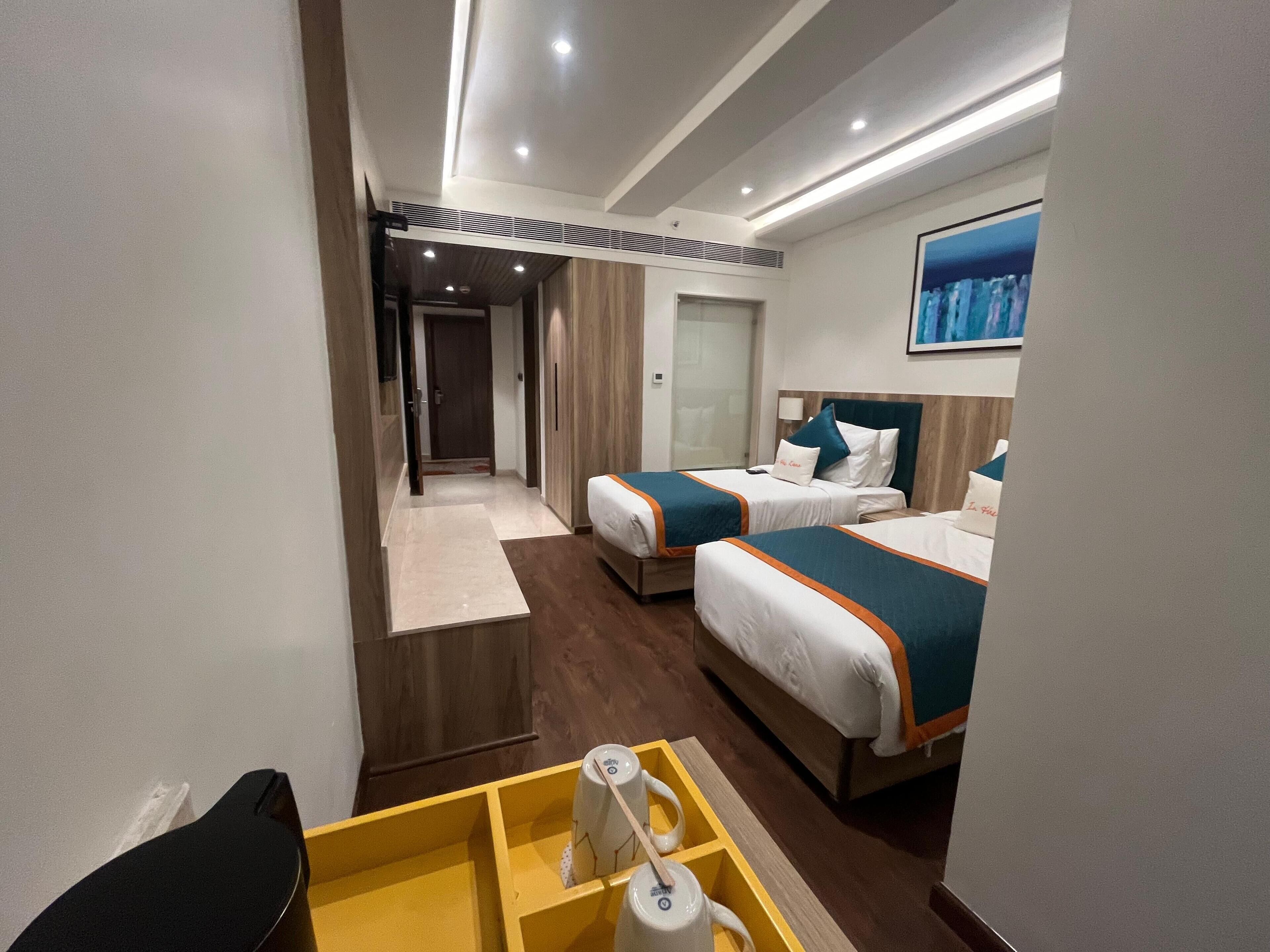 A hotel room with two beds, a small table with a cup and a remote control, and a painting on the wall.