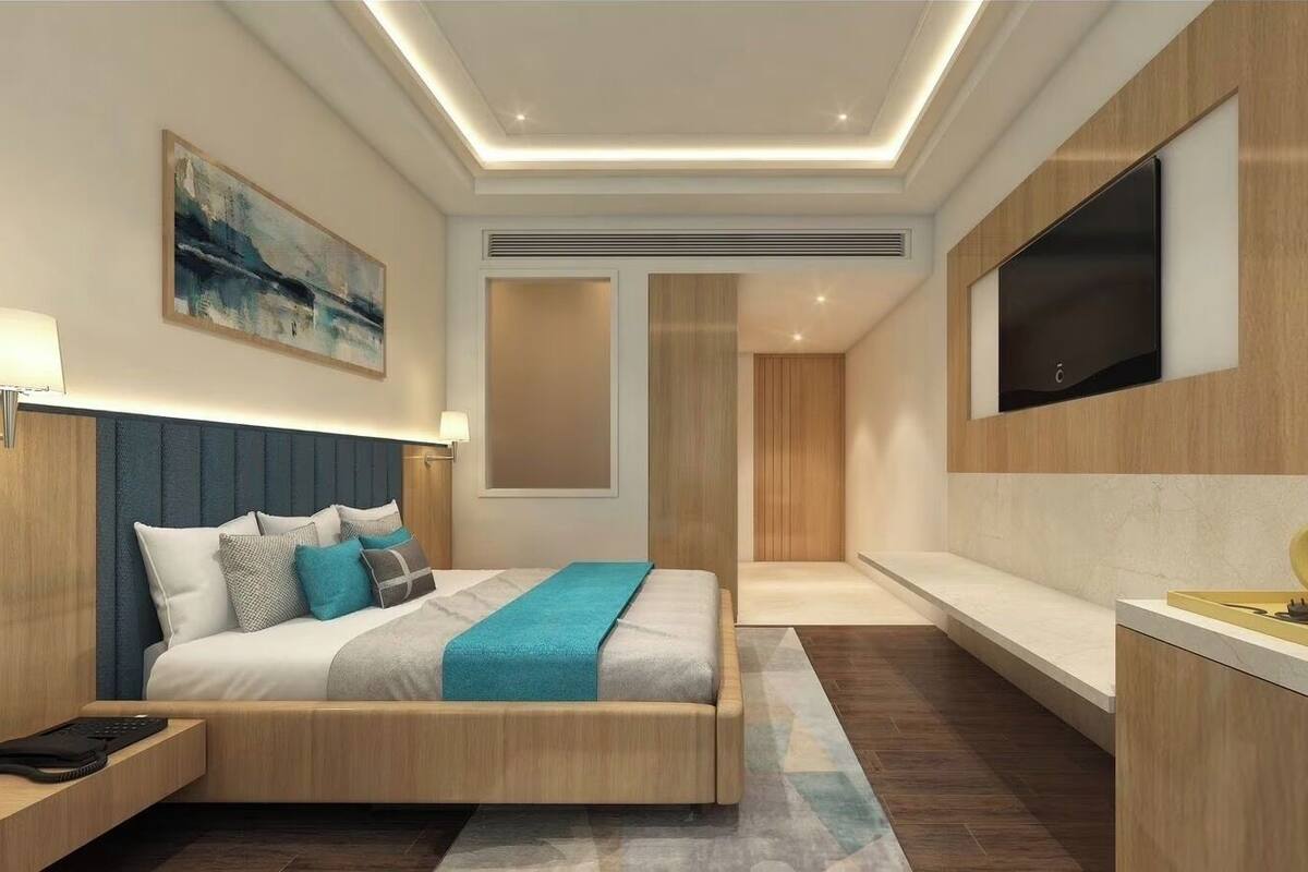 Une chambre d’hôtel moderne équipée d’un lit, d’une table de chevet, d’une lampe, d’œuvres d’art, d’une télévision et d’une machine à café.