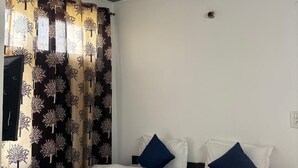 Ein Schlafzimmer mit einem Bett, zwei Kissen, einem Deckenventilator und gemusterten Vorhängen.