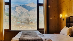 A bed with a quilt, a window with a view of mountains, and a wooden wall. - Ekaant Stays - Manali (Manali)