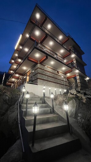 Un edificio de varios pisos con un diseño arquitectónico moderno, que destaca una escalera con escalones y barandillas iluminadas.