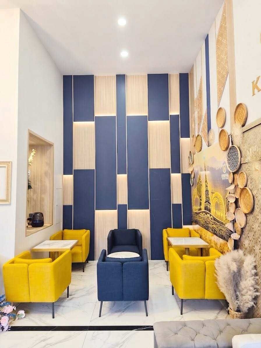 A modern interior with a geometric wall design, a central seating area with yellow and blue chairs, and a decorative wall with cultural artwork.