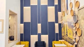 Un interior moderno con un diseño de pared geométrico, un área de estar central con sillas amarillas y azules, y una pared decorativa con arte cultural.