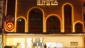 The exterior of Khota Hotel with a prominent sign, a covered entrance, and a parking area with a car.