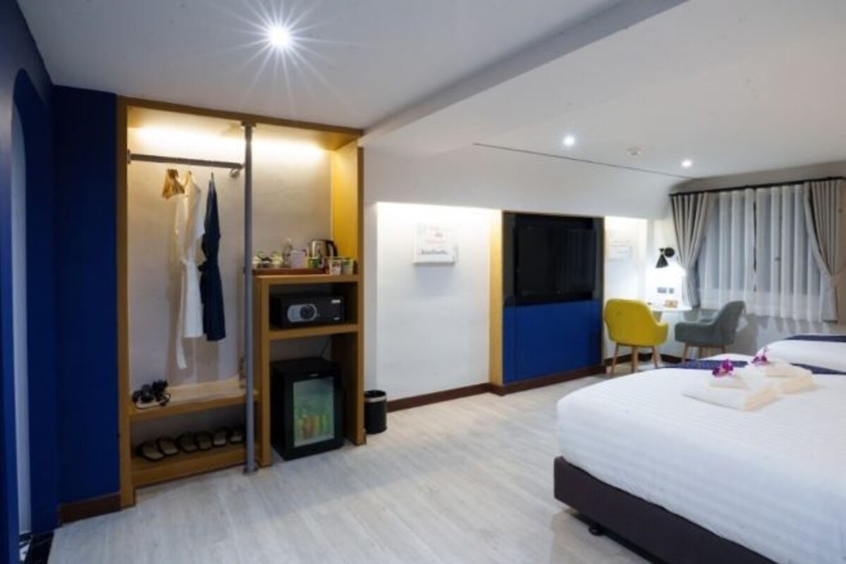 A hotel room with a bed, a desk, a chair, a wardrobe, and a small kitchenette.