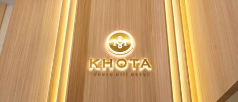 Pared de madera con el logotipo iluminado y el nombre "KHOTA" y el lema "photo hill hotel".