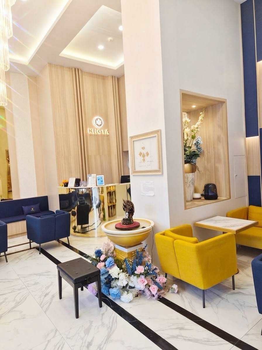 Een hotellobby met een receptiebalie, een zithoek en decoratieve bloemen.