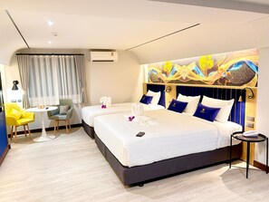 Quarto de hotel com uma cama grande, duas mesas de cabeceira, uma escrivaninha com cadeira e um ar-condicionado fixado na parede.