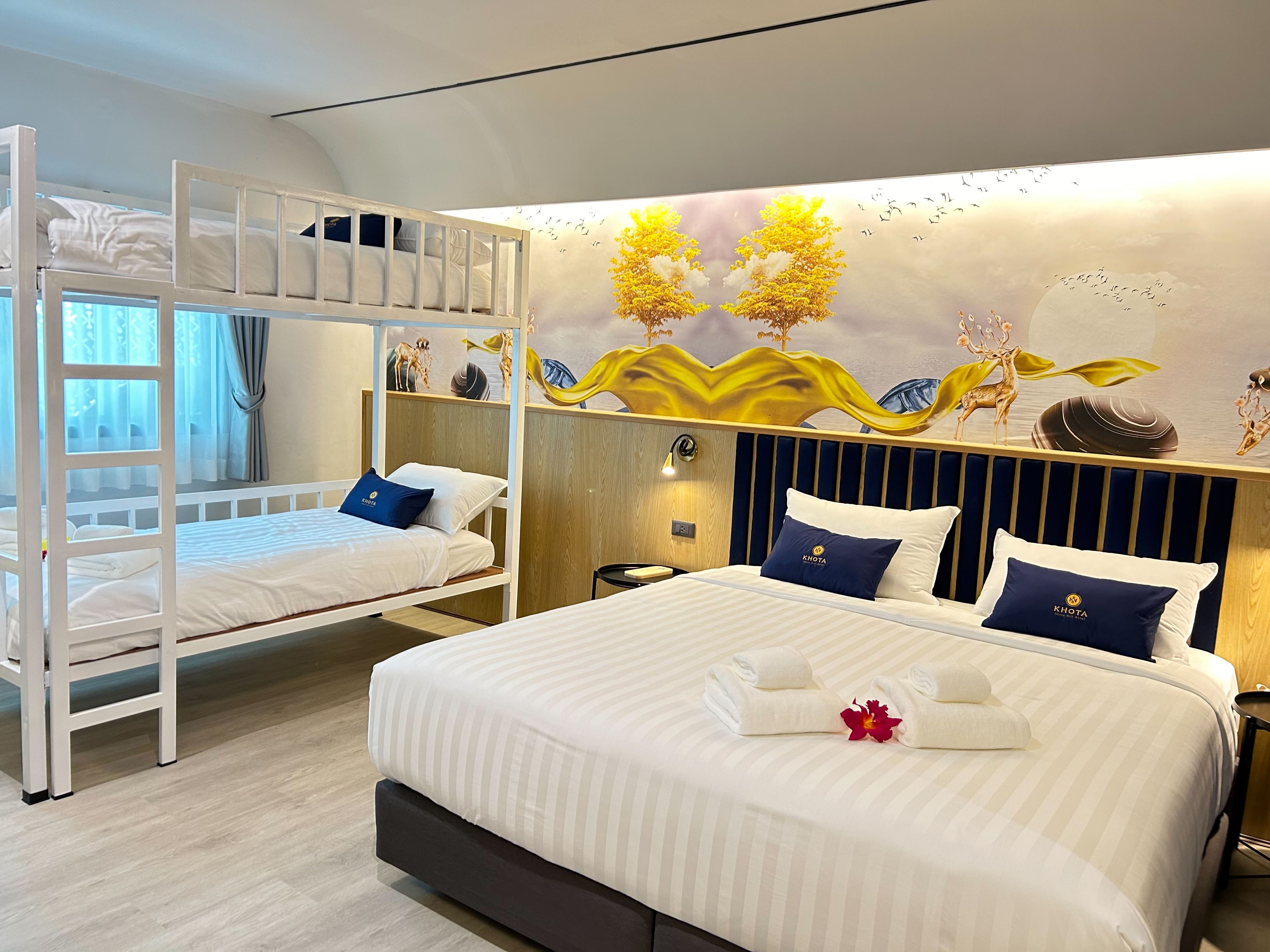 A hotel room with two beds, one with a bunk bed and the other a standard bed, both with white bedding and pillows.