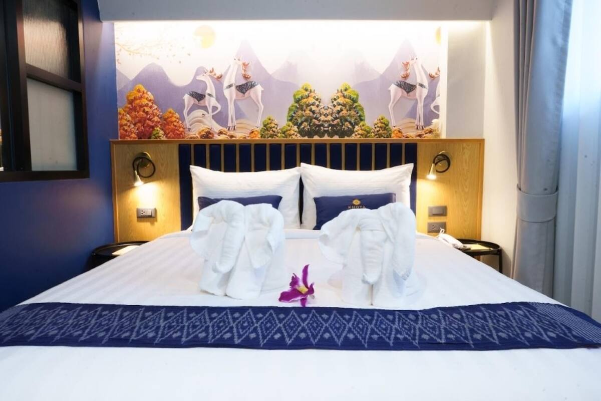 Una camera d'albergo con un letto grande, due cuscini, una testiera decorativa e un affresco sulla parete.
