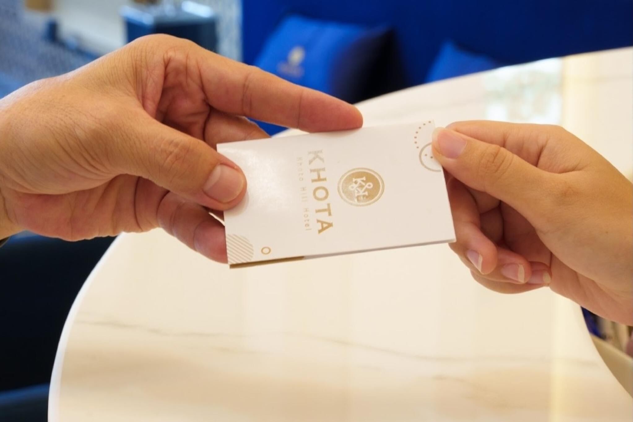A person holding a white envelope with the text "KHOTA HOTEL" and a logo.