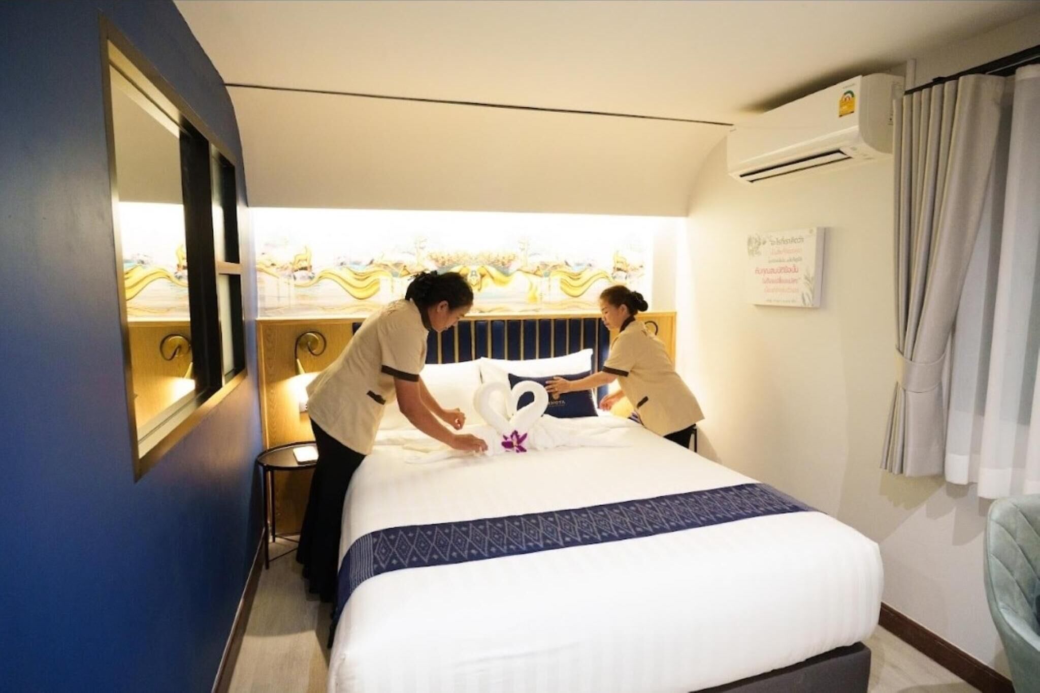 Une chambre d’hôtel avec un lit bien fait, une table de chevet et une fenêtre avec des rideaux.