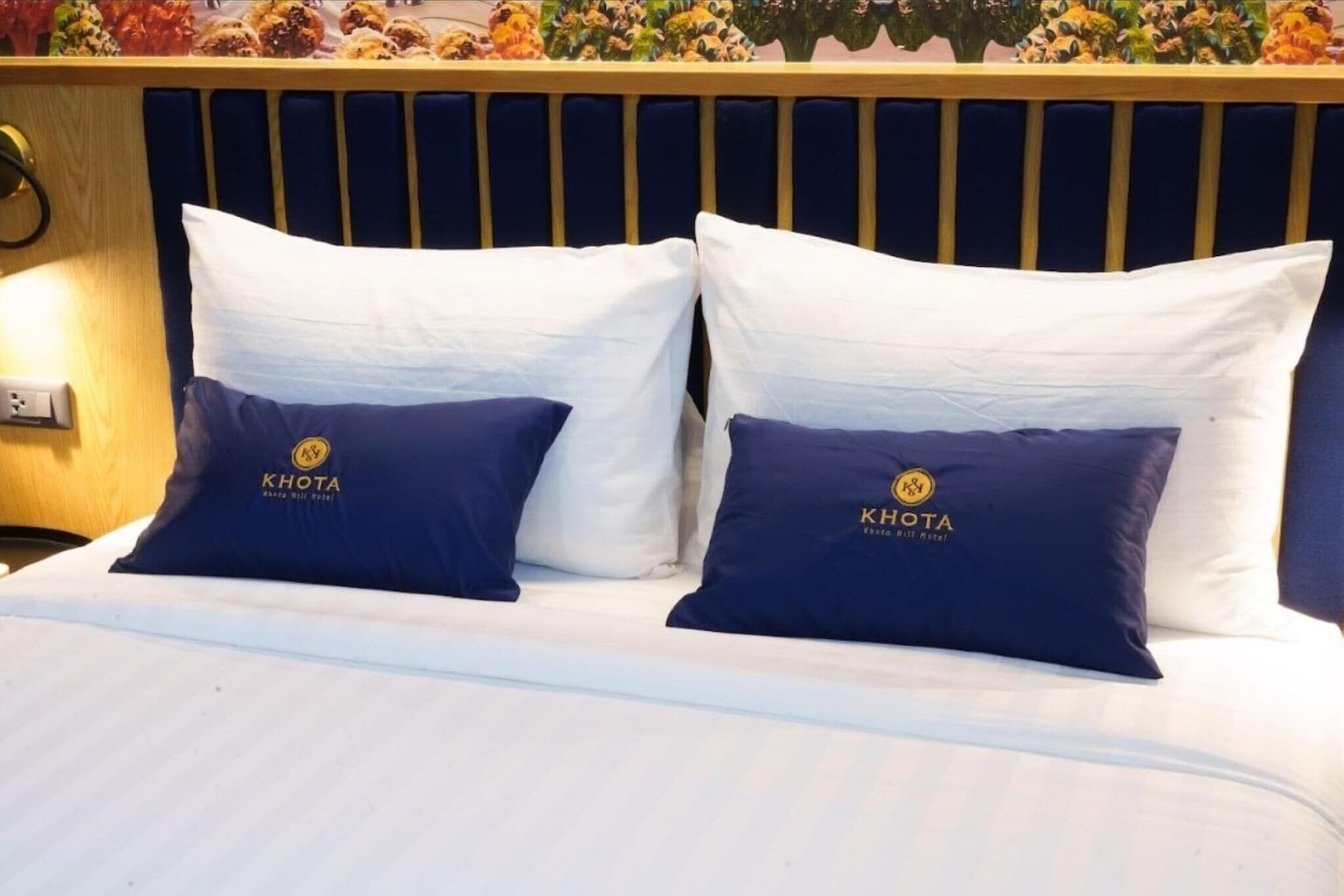 A bed with two pillows, one white and one navy blue, with a logo on the navy blue pillow.