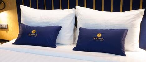 A bed with two pillows, one white and one navy blue, with a logo on the navy blue pillow.