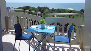 A balcony with a table set for two, chairs, a potted plant, and a view of the sea. - Apartment in Caorle Near Beach & Pool (Caorle)