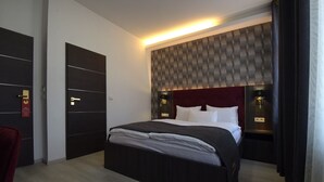 Et moderne hotelværelse med en stor seng, mørk træpanelling, en rød sengegavl og vægmonteret belysning.